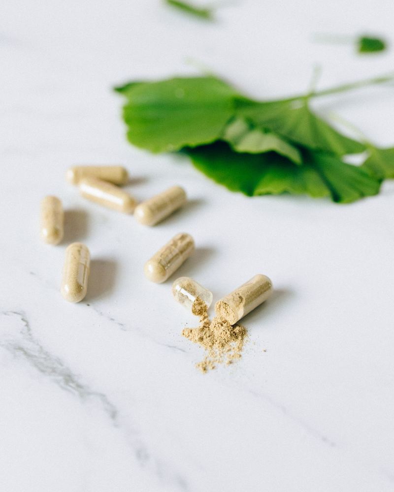 Plant-based capsules and a fresh green leaf on white marble