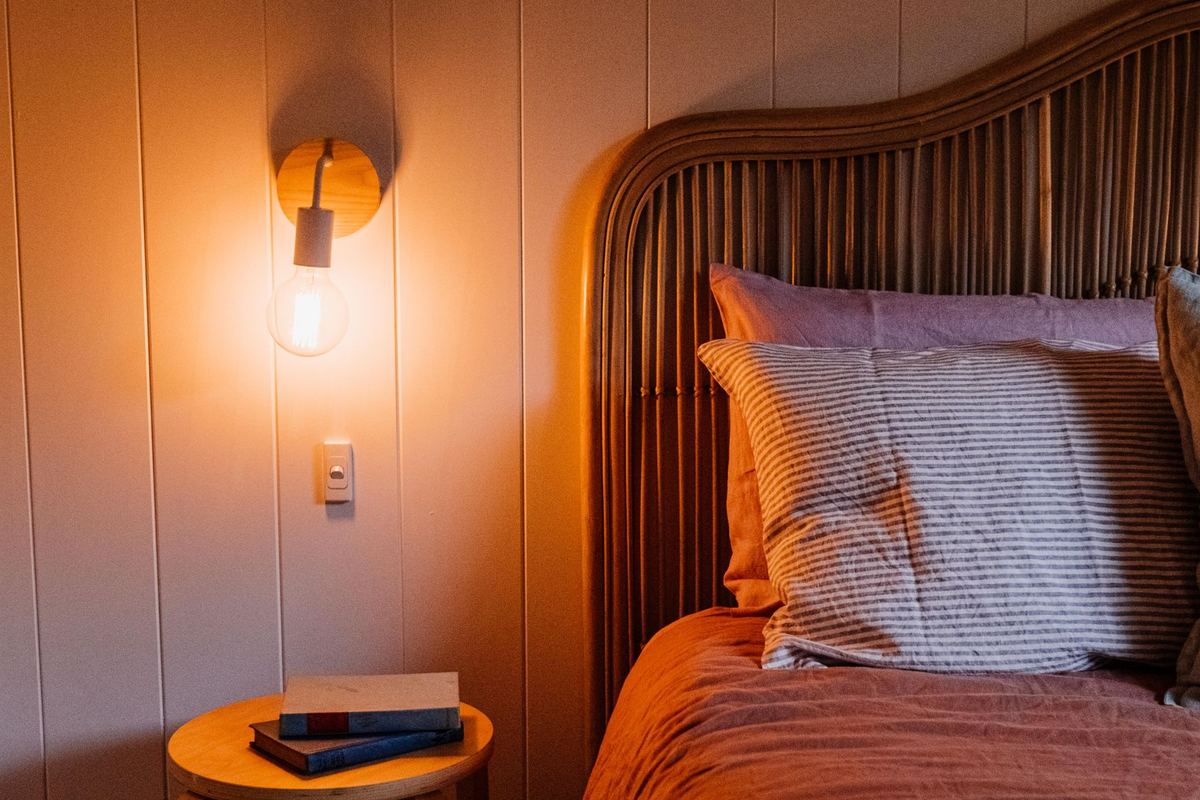 A softly lit bedroom with a warm wall lamp and a bedside stool