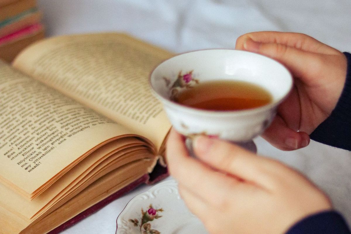 Hands holding a cup of tea over an open book